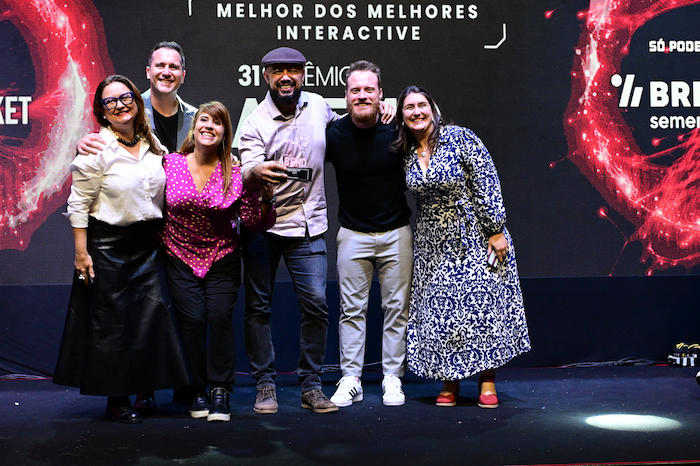 Equipe da HouseCricket comemorando no palco a conquista do Prêmio ABEMD 2025, reconhecimento nacional de excelência em marketing de dados e performance digital. A foto mostra seis profissionais sorridentes com o troféu em mãos, sob o letreiro “Melhor dos Melhores Interactive”, refletindo o espírito colaborativo e inovador da agência. Ao fundo, a atmosfera de celebração reforça o destaque da HouseCricket no cenário de marketing brasileiro.